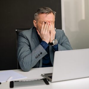 A businessman sitting at his desk with his head in his hands in frustration as he tries to deal with a commercial dispute, searching for resolutions on his laptop